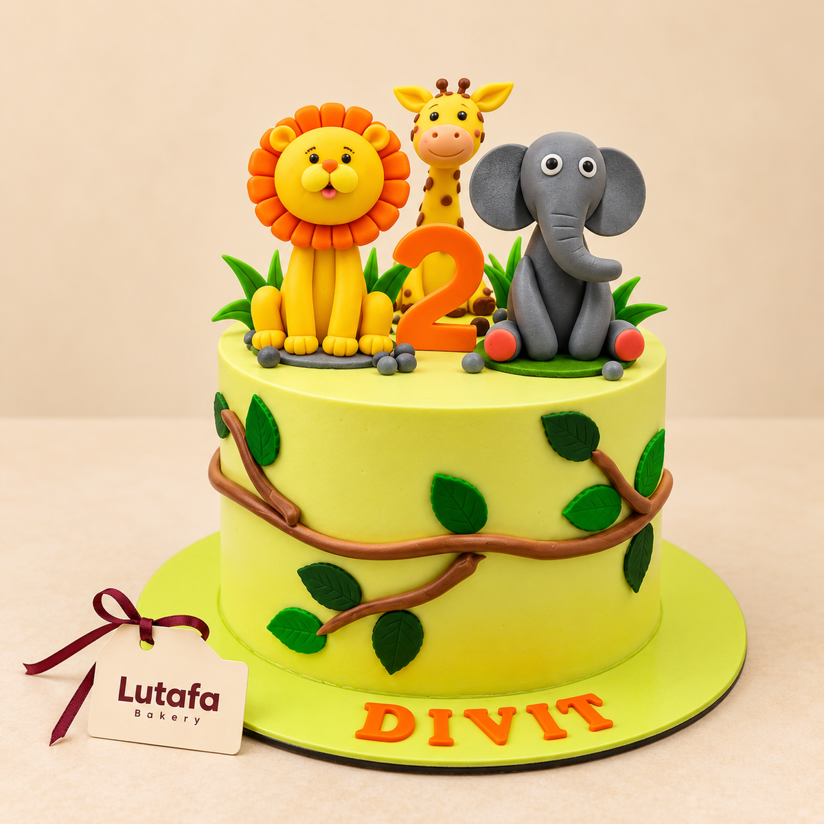A round yellow fondant cake decorated with green leaves and brown vine patterns, topped with a yellow lion, a giraffe, a gray elephant, and an orange number 2. The cake is displayed on a matching yellow cake board with the name 'DIVIT' in orange letters, and a 'Lutafa Bakery' tag is attached on the left.